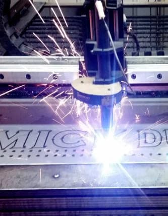 CNC plasma torch cutting lettering into a stainless steel plate, throwing sparks