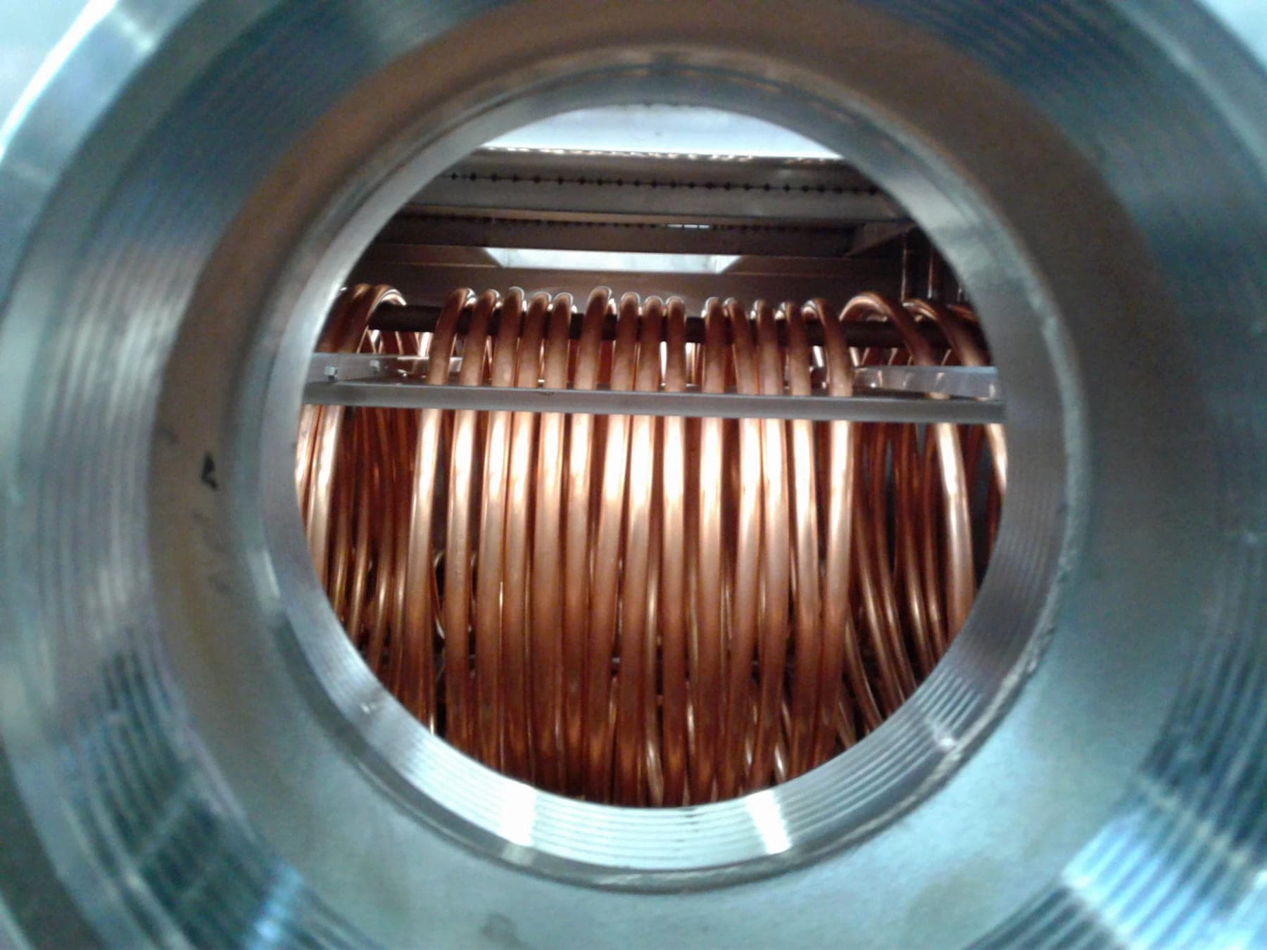 Copper heat exchange coils seen through a six-inch port in a stainless steel storage tank