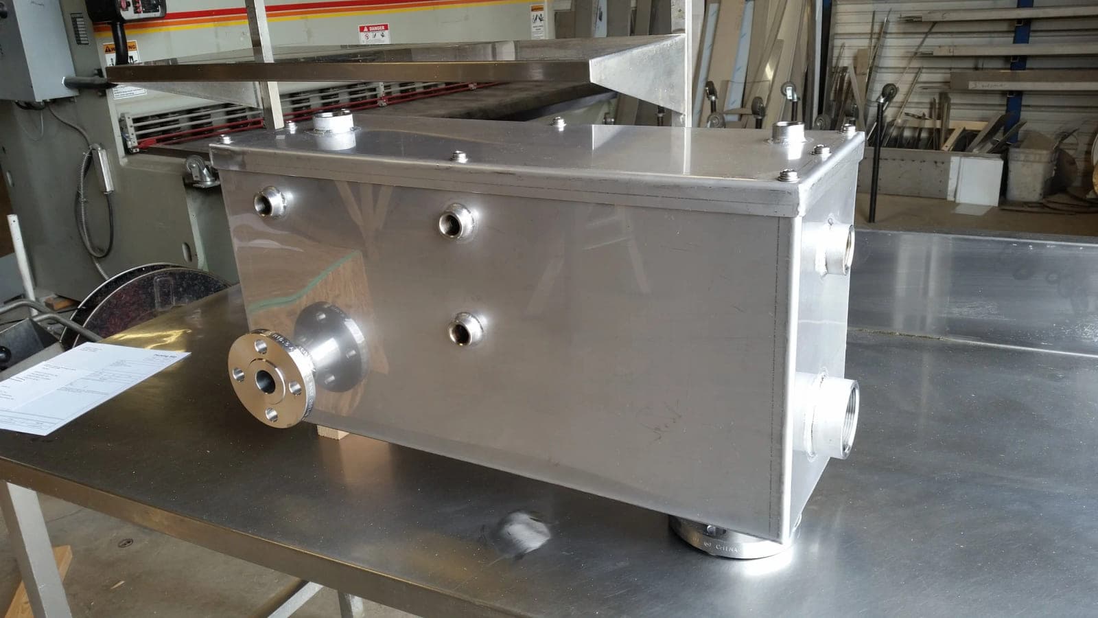Custom rectangular stainless steel vessel with threaded couplings and a flanged connection on a shop table