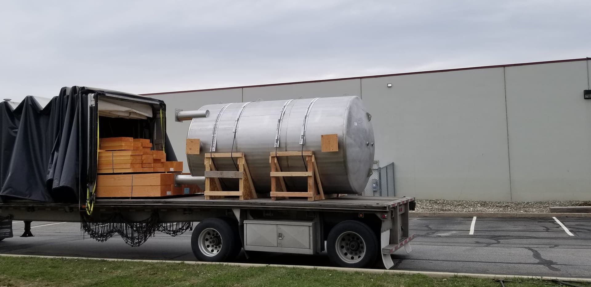 Horizontal stainless steel pressure tank cradled and strapped to a flatbed trailer