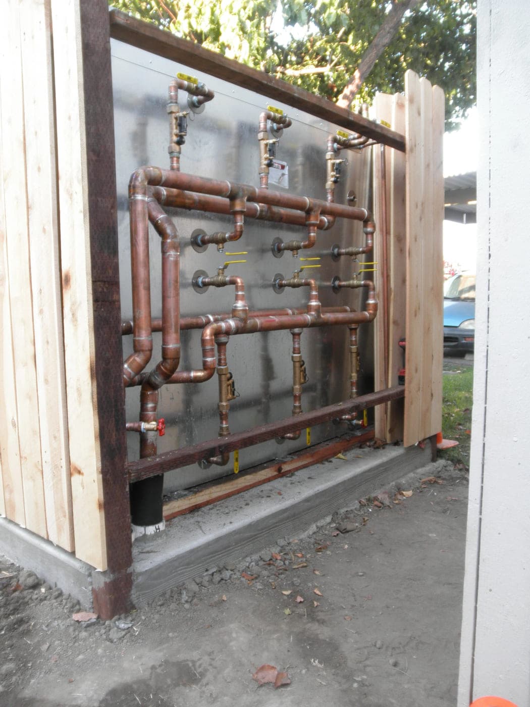 Rectangular stainless steel solar storage tank installed outdoors with a copper supply and return manifold