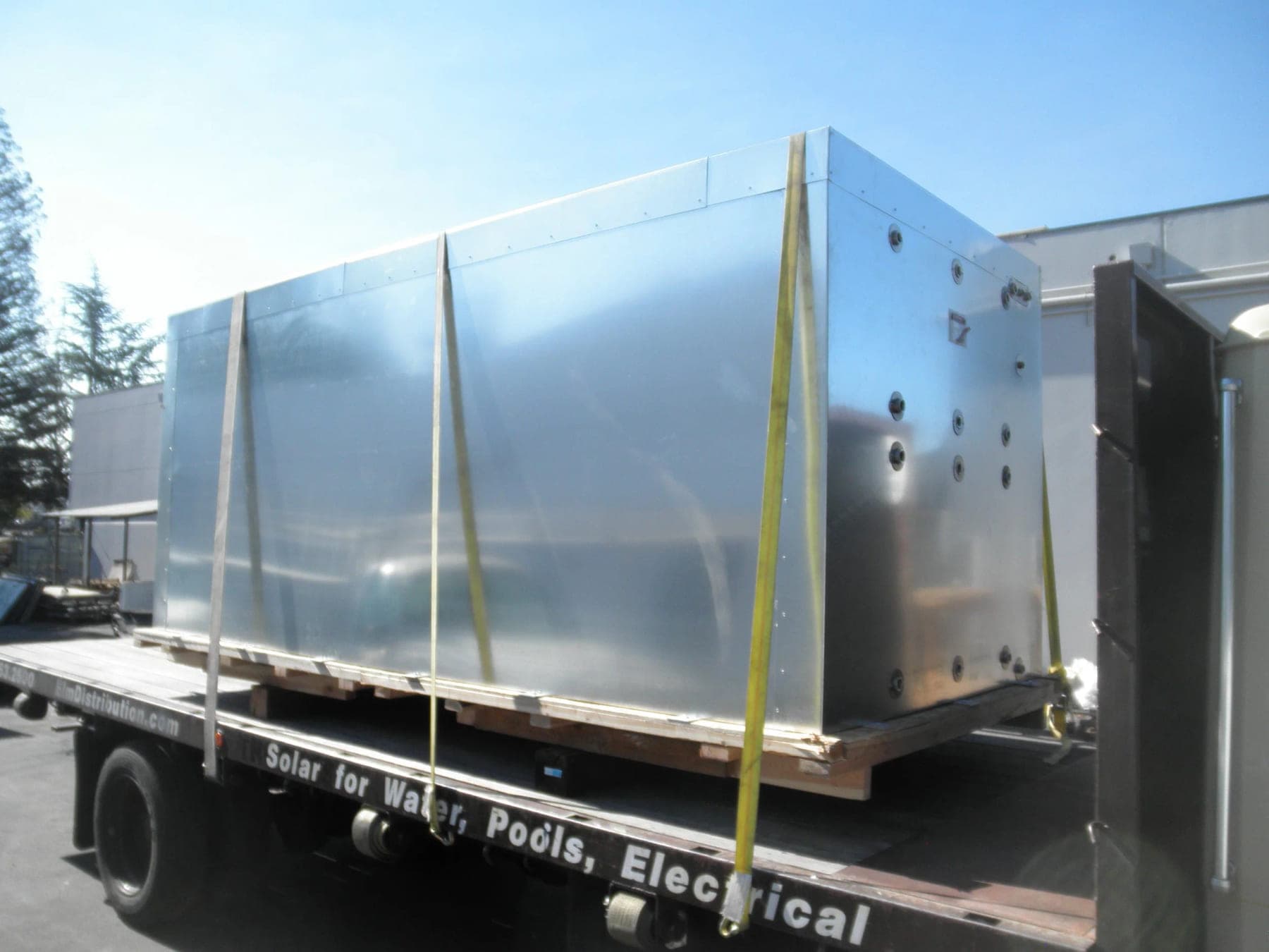 Large rectangular stainless steel storage tank strapped to a flatbed truck for delivery