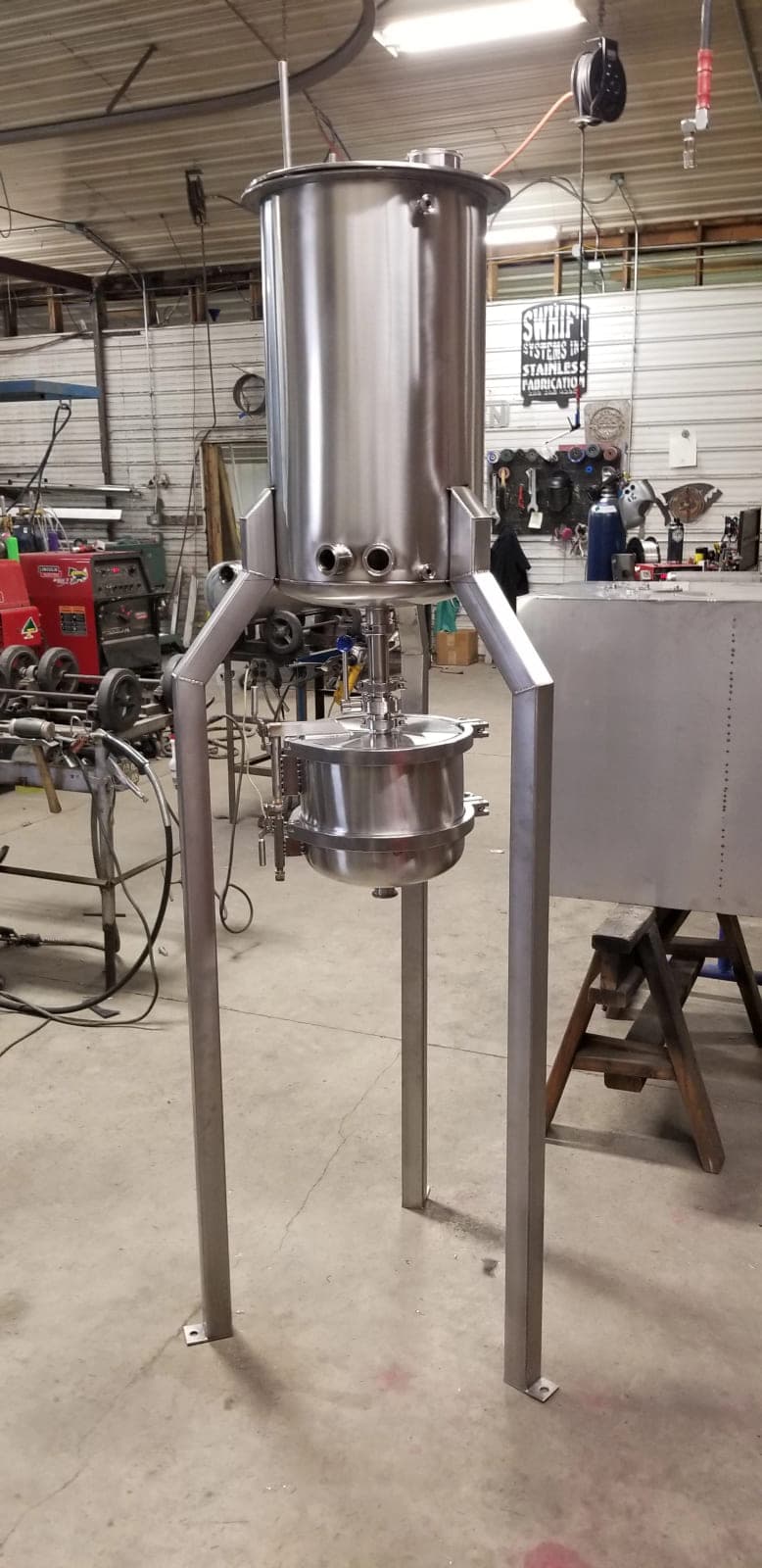 Stainless steel extractor vessel on tall legs above a clamped collection vessel in the Swhift shop