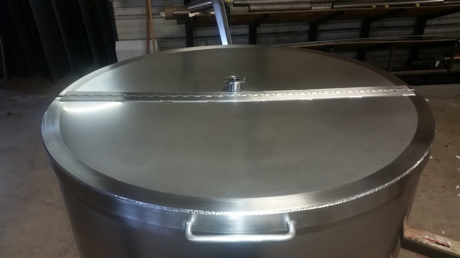 Large-diameter stainless steel tank with a hinged lid and sanitary fitting on the Swhift shop floor